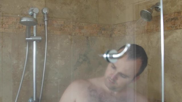 A dolly shot of a man washing hair in shower