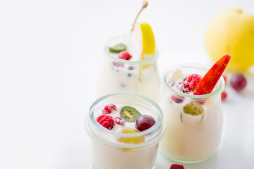 jars with yogurt and colorful fruits on a white background.