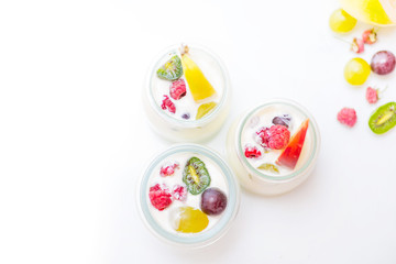 jars with yogurt and colorful fruits on a white background.