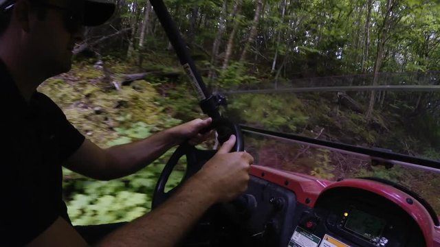 A wide shot of man steering a side by side vehicle in thick green forest