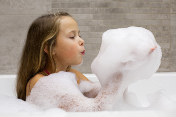 Cute little girl playing with foam in a bathroom