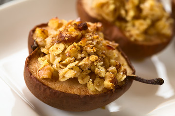 Sweet baked pear halves topped with a crisp crust of oatmeal, sugar and walnut, sprinkled with cinnamon, photographed with natural light (Selective Focus, Focus one third into the crumble on the pear)