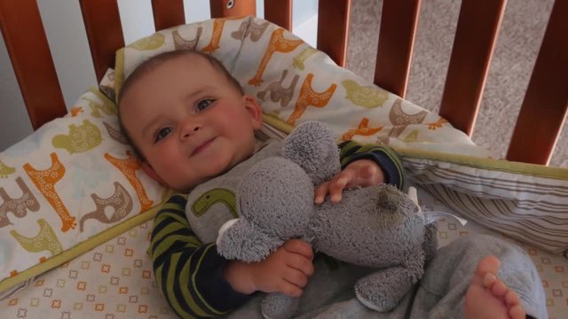 Cute baby boy with his big eyes in his crib in the room dolly shot