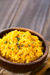 Pumpkin risotto prepared with pumpkin puree and sprinkled with fresh thyme leaves served in wooden bowl, photographed with natural light (Selective Focus, Focus one third into the risotto)
