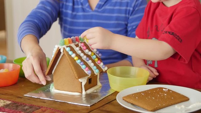 A mother and son decorating a gingerbread house