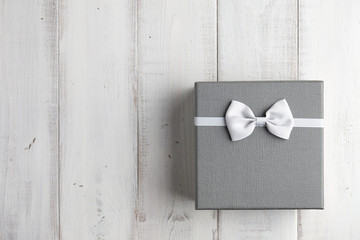 Strict gray gift box with white bow on wooden background