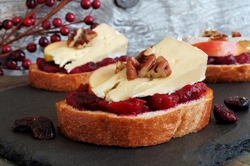 Crostini appetizers with cranberry sauce, apples, brie and pecans on slate server