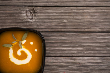 Delicious pumpkin soup with cream and green decoration on dark rustic wooden table. Top view