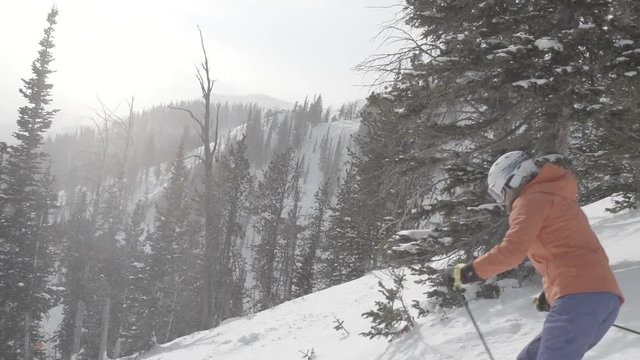 woman comes out of trees to ski fresh ski slope on mountain with a moving camera reveal behind trees