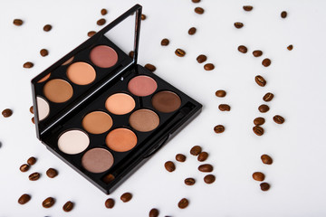 Decorative cosmetics and coffee beans over white background.