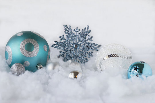 horizontal image of bright white and teal blue ornaments placed on a fake white snow with a white background with space for copy or text.