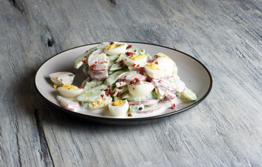 Radish - cucumber - quail egg salad, porcelain plate, grey background