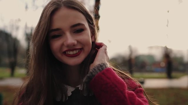 Attractive girl in red coat walking in the sunshine city and communicate via smart phone (phablet).