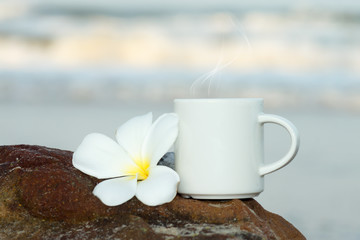 coffee cup and frangipani flowers on the beach