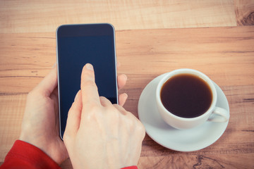 Vintage photo, Hand of woman touching blank screen of mobile phone, cup of coffee