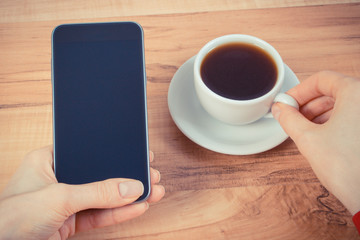 Vintage photo, Hand of woman touching blank screen of mobile phone, cup of coffee