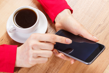 Hand of woman touching blank screen of mobile phone, cup of coffee