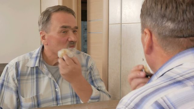 Senior man of shaving in the bathroom. It uses shaving foam and disposable razor. The concept of self-care