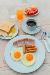 Breakfast with Fried egg, Ham, Sausage, toast, jam, butter, water melon, orange juice and black coffee on marble table.