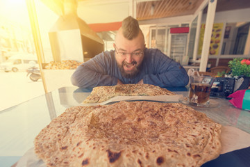 Bearded man with a mohawk eats Turkish Gozleme flat cake in cafe, sunny