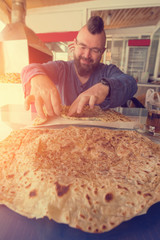 Bearded man with a mohawk eats Turkish Gozleme flat cake in cafe, sunny
