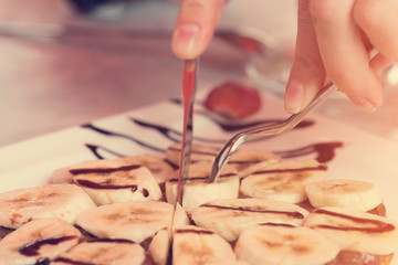 Woman eating with a fork and knife dessert with bananas and chocolate. Toned