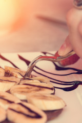 Woman eating with a fork and knife dessert with bananas and chocolate. Toned