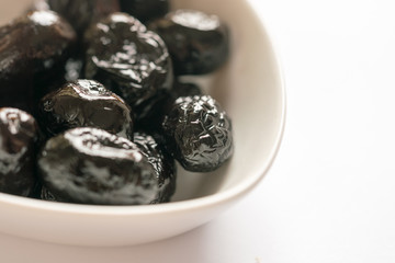 Small plate with black sun-dried olives in white plate on a white background