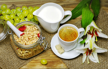 Breakfast with granola,warm milk,fresh bunch of grapes and a cup of espresso placed with beautiful lilies flower on wooden background.