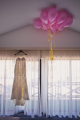 Wedding dress by the window and pink balloons