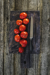 The ingredients for the sauce. Tomatoes and knife on dark vintage cutting board. Selective focus. Toned image