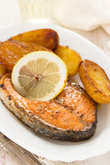 fried salmon with potato and lemon on white plate on wooden background