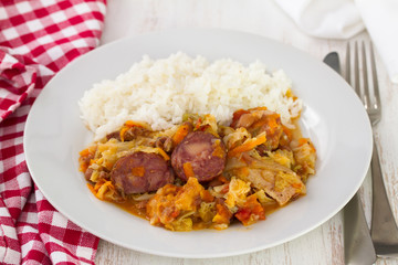 meat with sausages, cabbage and rice on white plate on wooden background