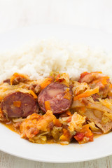 meat with sausages, cabbage and rice on white plate on wooden background