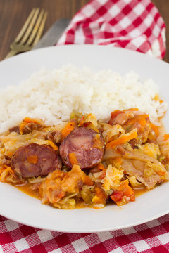 meat with sausages, cabbage and rice on white plate on wooden background