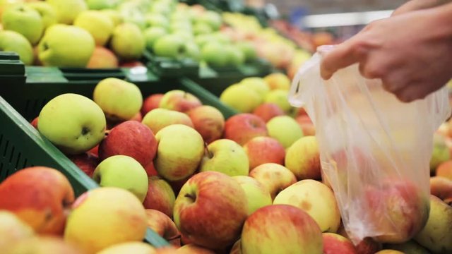 woman putting apple to bag at grocery store