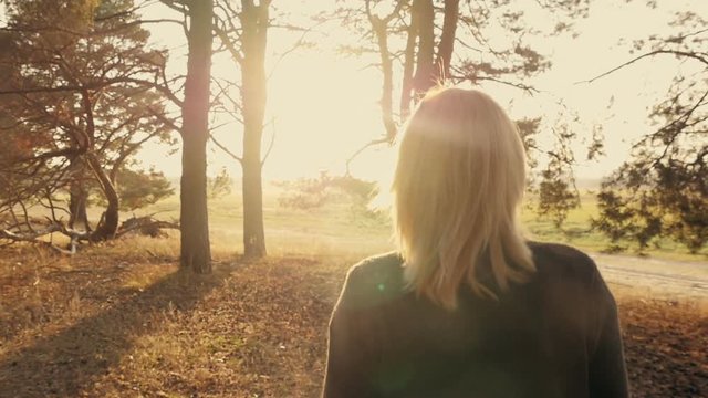 Blond girl walking in the forest at sunset