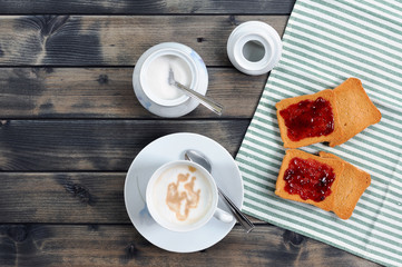 Foods of the Italian breakfast with coffee milk and rusks with jam on an old wooden table