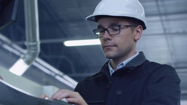 Engineer in Hard Hat Setting Up CNC Machine at the Factory. Shot on RED Cinema Camera in 4K (UHD)