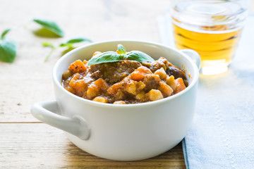 Beef stew with chickpeas and carrots in a white bowl on a wooden