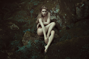 Fototapeta na wymiar Dark forest dryad posing on mossy rocks