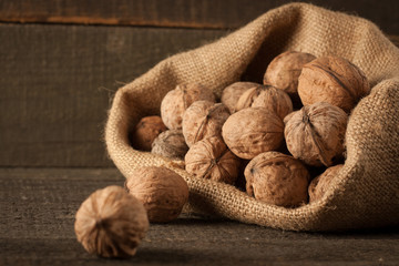 Walnut kernels in sack and whole walnuts on rustic old wood.