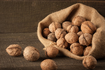 Walnut kernels in sack and whole walnuts on rustic old wood.