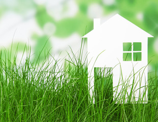 Small house from white paper in grass on abstract green.
