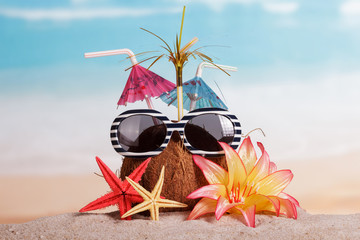 Coconut, sunglasses, starfish and flower in the sand against sea.
