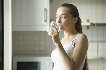 Portrait of a young attractive girl drinking water in the kitchen. Health care concept photo, lifestyle