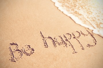 Fototapeta na wymiar Be happy written on sand