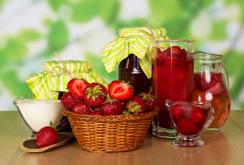 Basket strawberries, spoon, jars jam, beverages, cream on abstract green.