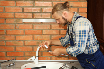 Handsome plumber repairing faucet in kitchen