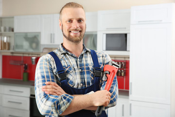 Portrait of handsome plumber with pipe wrench in kitchen